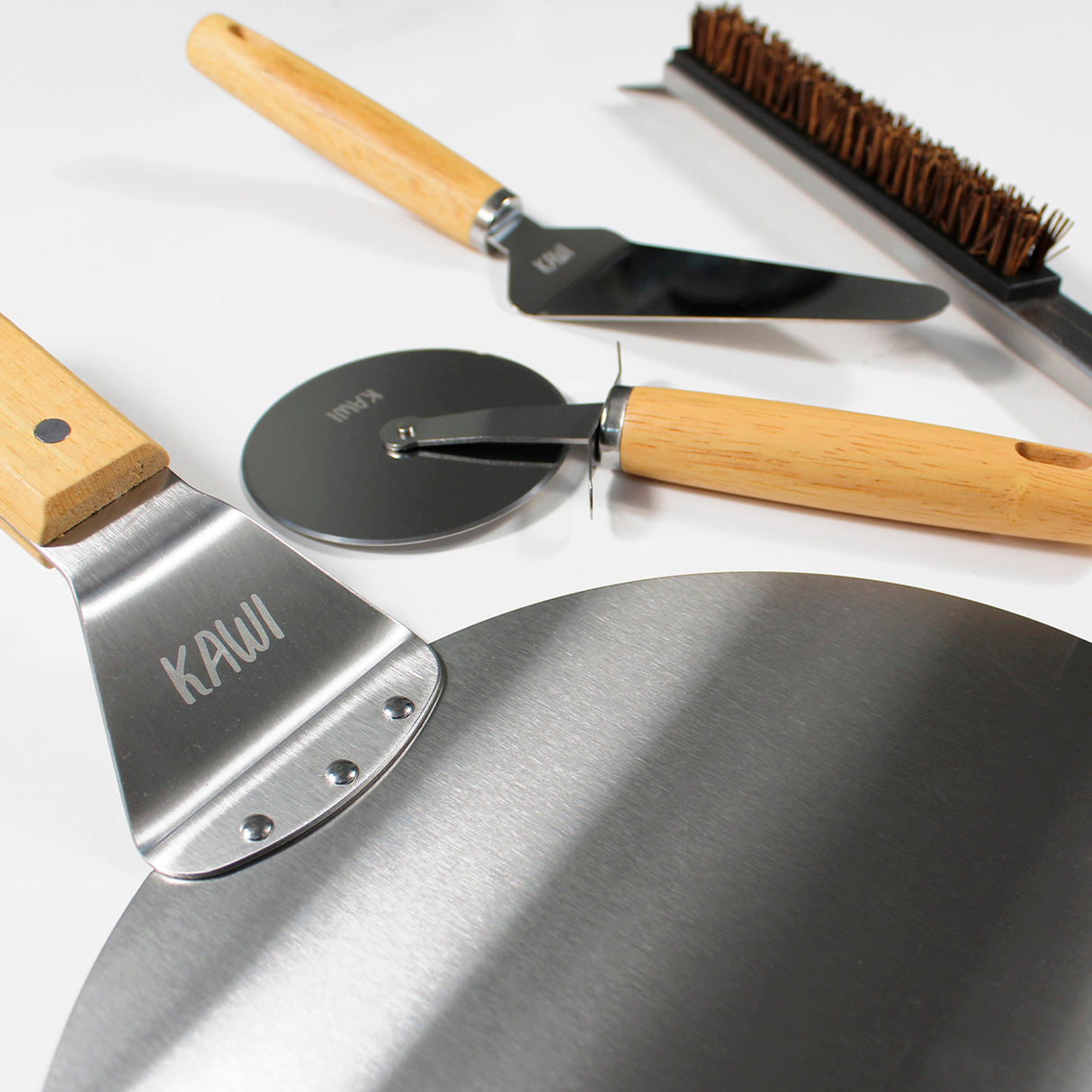 Set para pizza Kawi Pizzaiolo de 4 piezas: cortador, pala, cepillo y espátula. Acero inoxidable y madera. ¡Prepara y sirve pizza como un profesional! Compra online, envío a Chile.